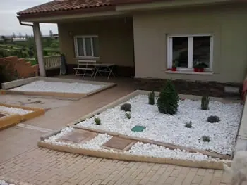 Parterres de grava blanca con plantas aromáticas frente a una vivienda